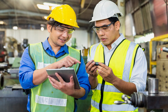 A Skilled Mechanic In A Metal Lathe Is Checking Parts On A Tablet. Engineers Are Working And Repairing Machines In Industrial.