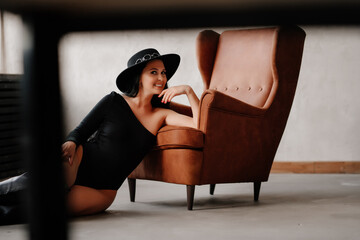 woman with dark hair in black bodysuit and hat on floor of leather chair