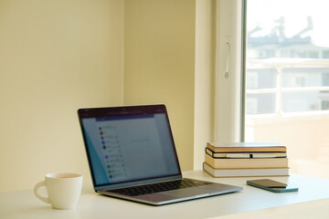 Home office concept. Designated work from home area near the window. Modern laptop, notebook and vase with flowers on table. Close up, copy space, background.