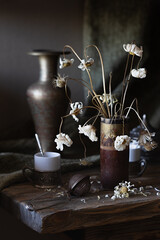 Vintage still life with withered daisies in a wooden vase and tea cups on an old wooden table.