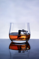 glasses of whiskey with ice cubes on black glass surface