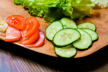 lettuce, ringed tomato and cucumber on a wooden cutting board.