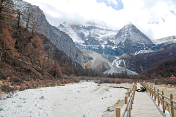 Landscape Long wood bridge to Pearl Lake with Chenrezig (Xiannairi) Holy snow Mountain background at Yading winter season. It is the highest peak in Daocheng Country,China - hikes to epic mountains 