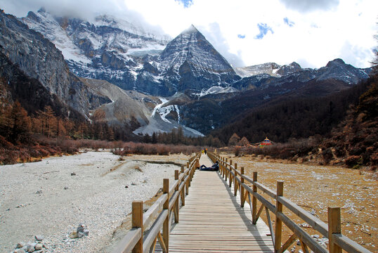Landscape Long wood bridge to Pearl Lake with Chenrezig (Xiannairi) Holy snow Mountain background at Yading winter season. It is the highest peak in Daocheng Country,China - hikes to epic mountains 