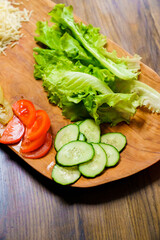 lettuce, ringed tomato and cucumber on a wooden cutting board.