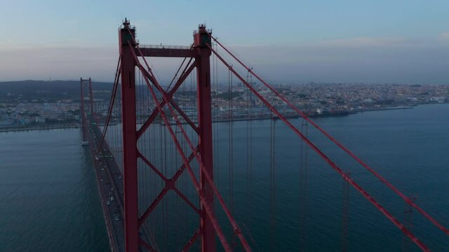 Aerial orbit of large red Ponte 25 de Abril bridge with car traffic crossing the sea on the coast of Lisbon, Portugal