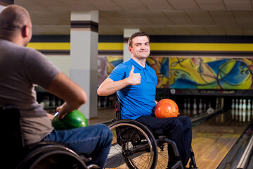 Two young disabled men in wheelchairs playing bowling in the club