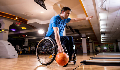 Fototapeta na wymiar Young disabled man in wheelchair playing bowling in the club