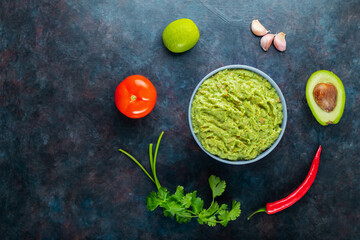 Fototapeta na wymiar Guacamole bowl with ingredients. Guacamole sauce and chili pepper, lime, avocado, parsley, garlic, tomato on a dark background. Mexican food. Copy space. Top view