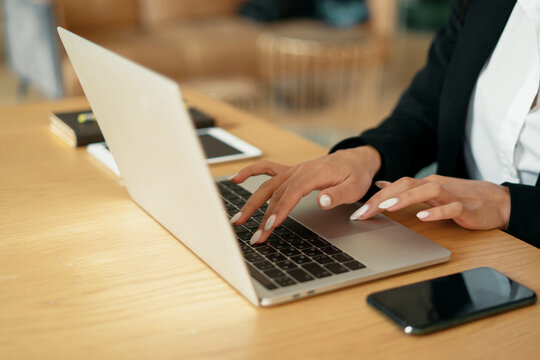 Confident business woman smiling afro appearance sitting in the office in a formal suit. It works by printing a message to the client on a laptop in a coworking space.