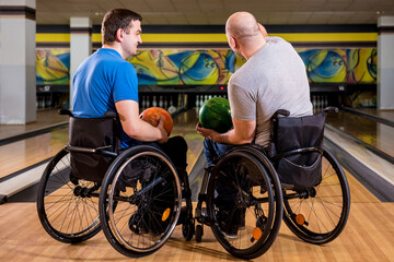 Obraz premium Two young disabled men in wheelchairs playing bowling in the club