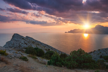 Sudak, Crimea - a view from Cape Meganom. Sunset sky with beautiful clouds. The Black Sea and the ridge of the Crimean mountains in the rays of the evening sun.