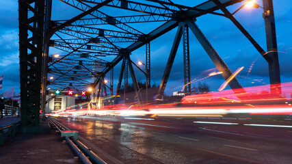 Fototapeta na wymiar Light trails from cars run across the bridge at dusk, at twilight time, traffic is chaotic.