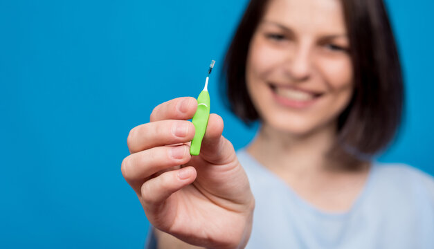 Beautiful happy young woman using interdental brush on blue background
