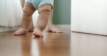 Asian Mother holding her little baby learning to walk on wooden floor at home. Cute toddler...