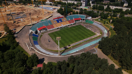 Football stadium in the city park. A new arena is being built nearby. A green field and stands are visible, painted in different colors. Aerial photography.