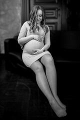 A happy pregnant woman sits on a chair and caresses her stomach. Mom Is Expecting A Baby. The Belly Of A Pregnant Woman. Pregnancy. Beautiful Pregnant Woman. The concept of motherhood.