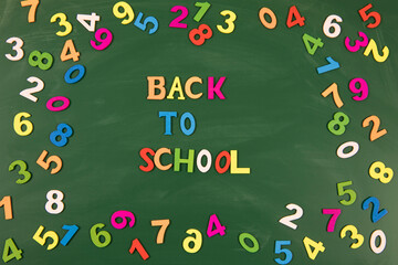 Background.Colorful inscription Back to school on a green school board in the center of the frame. Numbers of different colors are scattered around the text. Close-up, flat lay, horizontal. Education 