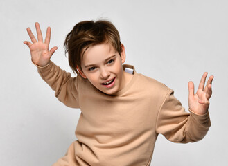 Cute little preteen boy child wearing fashion sportswear with raised hand want to scare standing on studio copy space background looking and shouting at camera. Children emotion and expression concept