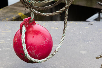 Eine rote runde Markierungsboje hängt an einem  aufgerollten Seil an einem Geländer.