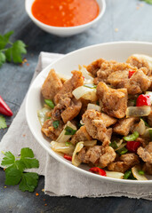 Stir fry chinese salt and pepper chicken with red, green chilli, onion, spring onion in white bowl.