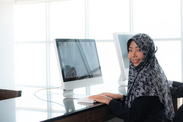 Smiling Young beautiful Muslim women in hijab wearing microphone headsets is working as customer care operator and team support information in call center office.