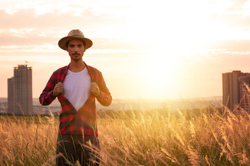 Farmer with hat in farm opening the shirt like superman plantation on sunset. Buildings and city blurred background. Space for text.