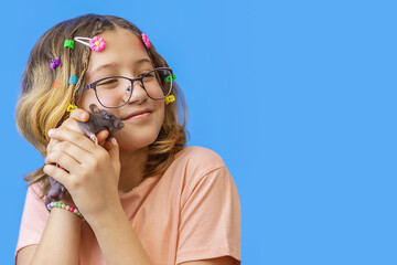 beautiful girl with glasses holds pet rat in her hands on blue background, love for rodents or animals, place to copy space