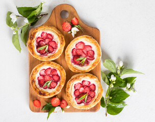 Dessert, small open pies made of puff pastry with cottage cheese and fresh strawberries on a wooden board on a white background top view