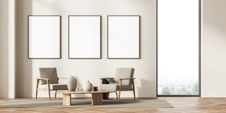 Three framed mockup posters in villa living room design interior, beige furniture on bright wall, wood floor, Two armchairs. Concept of relax.