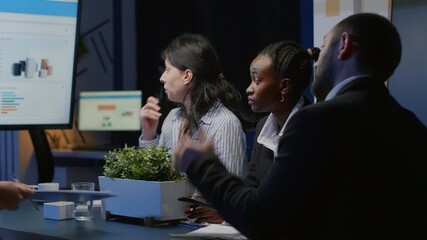 Multi ethnic businesspeople working in company meeting office room brainstorming management strategy late at night. Entrepreneur woman presenting business financial graphs on monitor