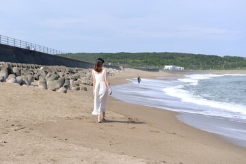 海岸を散歩する白いワンピース姿の若い女性