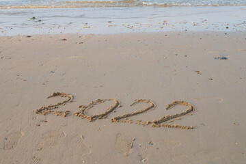Happy Christmas and New Year 2022 in sandy number on sea shore with ocean blue background