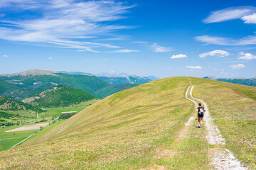 Naklejka premium Hiking in the Montelago highlands, Marche, Italy. Woman walking in green landscape unique hills and mountains landscape. Summer outdoors activity.