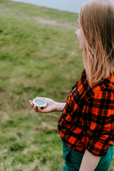 A girl in a red checkered shirt holds a compass in her hand, orienteering, the concept of finding a goal, a hipster woman walks in the woods