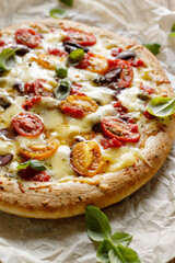 Close up view of the vegetarian pizza with cherry tomatoes, kalamata olives and fresh basil light background.