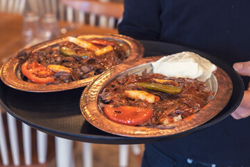 Waiter holding Iskender Kebab plates with food serving guests in a restaurant.