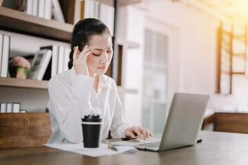 Pretty businesswoman sitting at her desk with a laptop computer with serious stress and headache with her hand kicking her head, concept of stress and boredom at work.