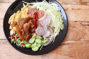 Shrimp Paste Fried Rice with shallot, sweet pork, fried egg, vegetable, and spicy chili on the black dish, and spoon, fork, top view, Thai traditional delicious food on wooden background closeup.