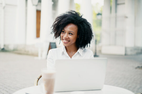 Student man on the street working on a laptop. Writes a message to the client by email. Blogger curly-haired young woman of African-American appearance near a business center in the city.