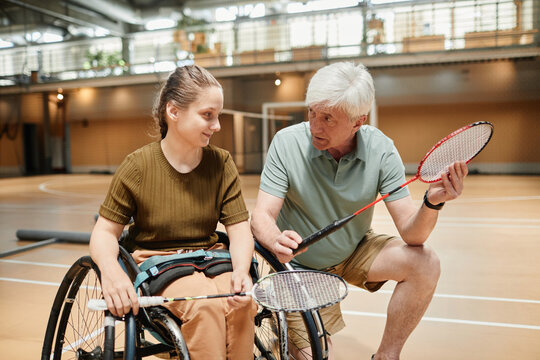 Portrait of smiling young woman in wheelchair talking to coach during badminton practice at sports court