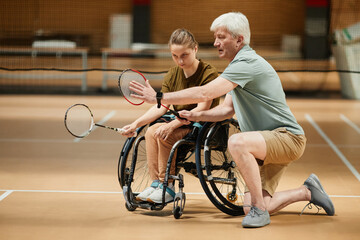 Full length portrait of mature coach training young woman in wheelchair at badminton practice in...