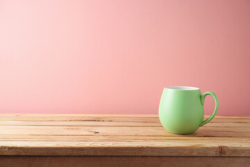 Green coffee cup on wooden table over pink background