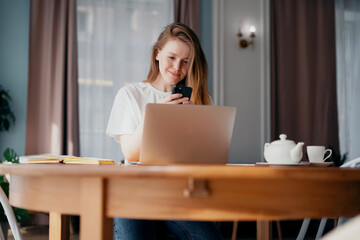 Distance learning at the Institute. Young red-haired woman freelancer. A smart student learns at home online via the internet. On a wooden table stands a laptop in the hands of a tablet.