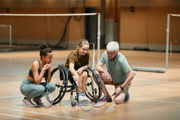 Fototapeta na wymiar Full length portrait of mature coach talking to young woman in wheelchair during badminton practice in sports court, copy space