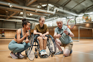 Fototapeta na wymiar Full length view at senior coach talking to young woman in wheelchair during badminton practice in sports court, copy space