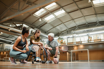 Senior coach talking to young woman in wheelchair during badminton practice in sports court, copy space