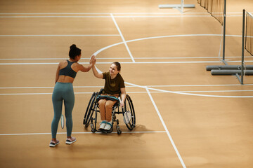 Wide angle view at smiling young woman in wheelchair playing badminton and high five partner during...