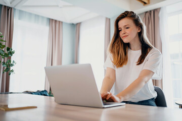 Fototapeta premium A confident female blogger of European appearance sits at home making an online order. The freelancer prints a message to the client on the tablet. Distance learning. A cozy place to work.