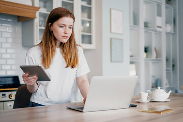 Calculates the credit in the online table. A female student works at home on a tablet. Prints a message in the social network communication on the computer. Online distance learning via video link.